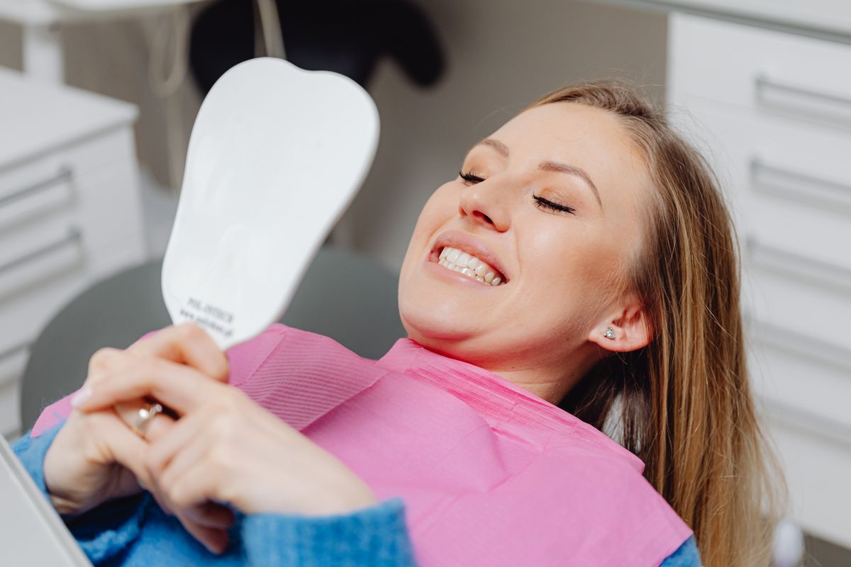 smile designing in Belapur — La Pearl Dental Boutique patient smiling with a hand mirror after aesthetic dental care